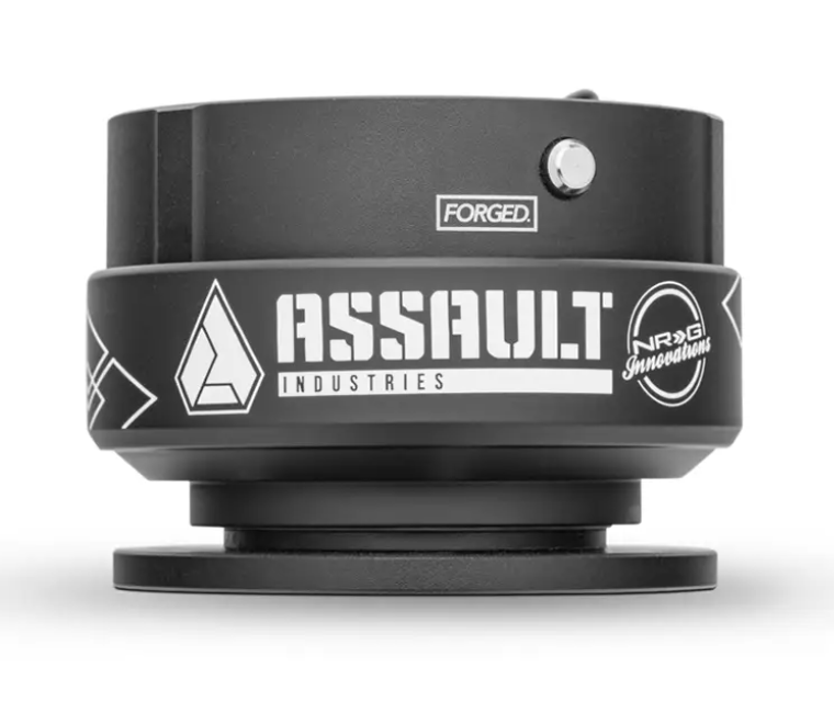 The 6 Bolt Universal Quick Release Steering Wheel Adapter features a black, round design with bold white ASSAULT INDUSTRIES and NRG Innovations logos, a geometric emblem, FORGED text on the side, metallic button, and matte finish. Hub not included.