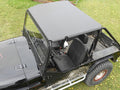 A Mahindra Roxor Sport Aluminum Top, black with an open back, large off-road tires, metal side steps, and a roll cage is parked on grass with yellow flowers scattered around. The vehicle features two front seats.